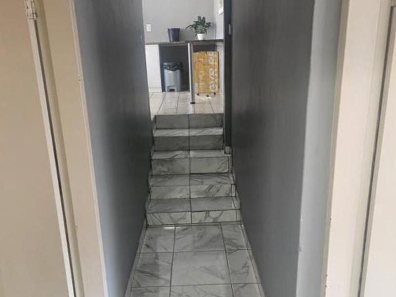A narrow hallway featuring marble-look tiled flooring and a small staircase leading to an adjacent room with dark grey wall finishes.