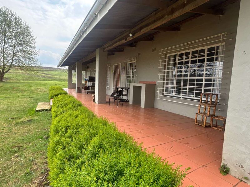 A covered outdoor patio featuring tiled flooring, a built-in braai, and security bars on windows, overlooking a spacious green lawn.