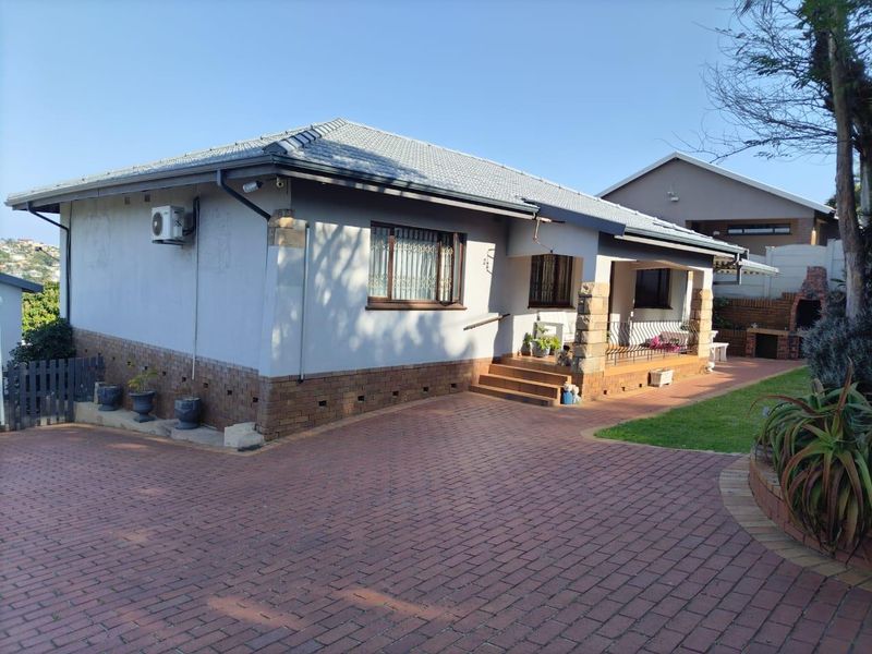 Front view of a well-maintained house featuring a paved driveway, tiled roof, stone-clad entrance pillars, and a built-in outdoor braai area.