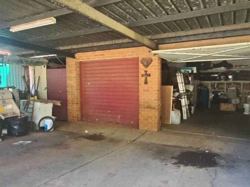 A functional garage space featuring a corrugated metal roof, brick walls, and a roll-up door, providing covered parking and storage area.