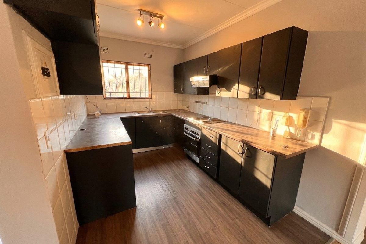 A functional kitchen featuring dark cabinetry, laminate countertops, a built-in oven with extractor fan, and tiled backsplash with wood-look flooring.