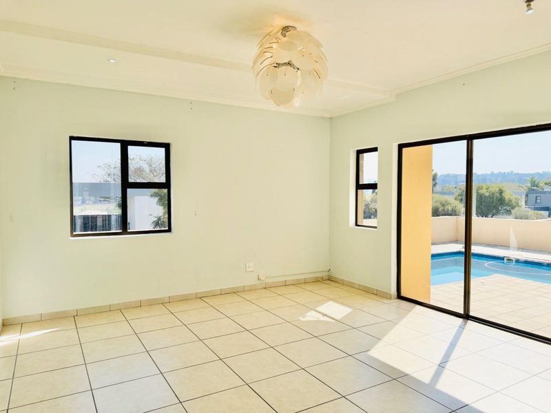 Bright and spacious living area featuring neutral tiled flooring, large windows, and sliding glass doors providing direct access to the outdoor pool area.
