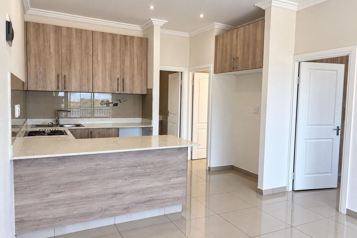 Modern kitchen featuring light wood-grain cabinetry, stone countertops, a built-in hob, and polished tile flooring in an open-plan layout.