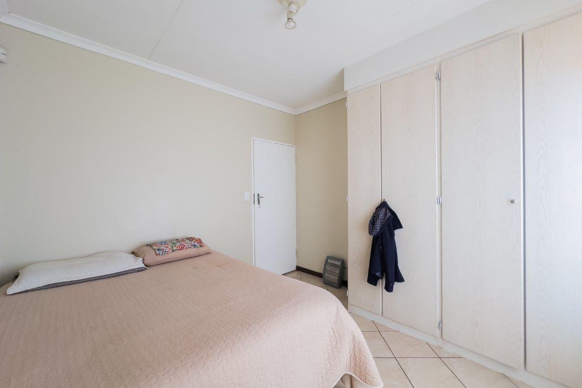 A bedroom featuring built-in cupboards with light wood-grain finish and tiled flooring.