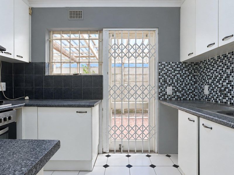 A functional kitchen featuring white cabinetry, dark laminate countertops, a built-in oven, and a security gate leading to the exterior.