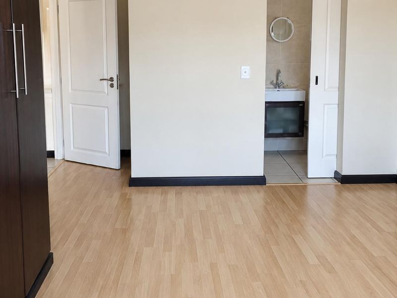 A clean, empty bedroom featuring light laminate flooring, built-in cupboards, and direct access to an en-suite bathroom with a vanity basin.