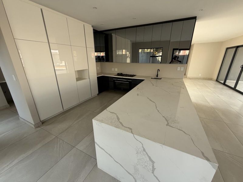 Modern kitchen featuring a large stone island, integrated cabinetry, built-in oven, gas hob, and sleek tiled flooring in an open-plan layout.