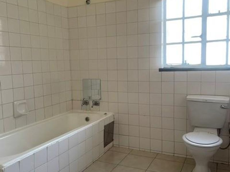A dated bathroom featuring a tiled bathtub, ceramic toilet, and full-height wall tiling, offering a blank canvas for renovation.