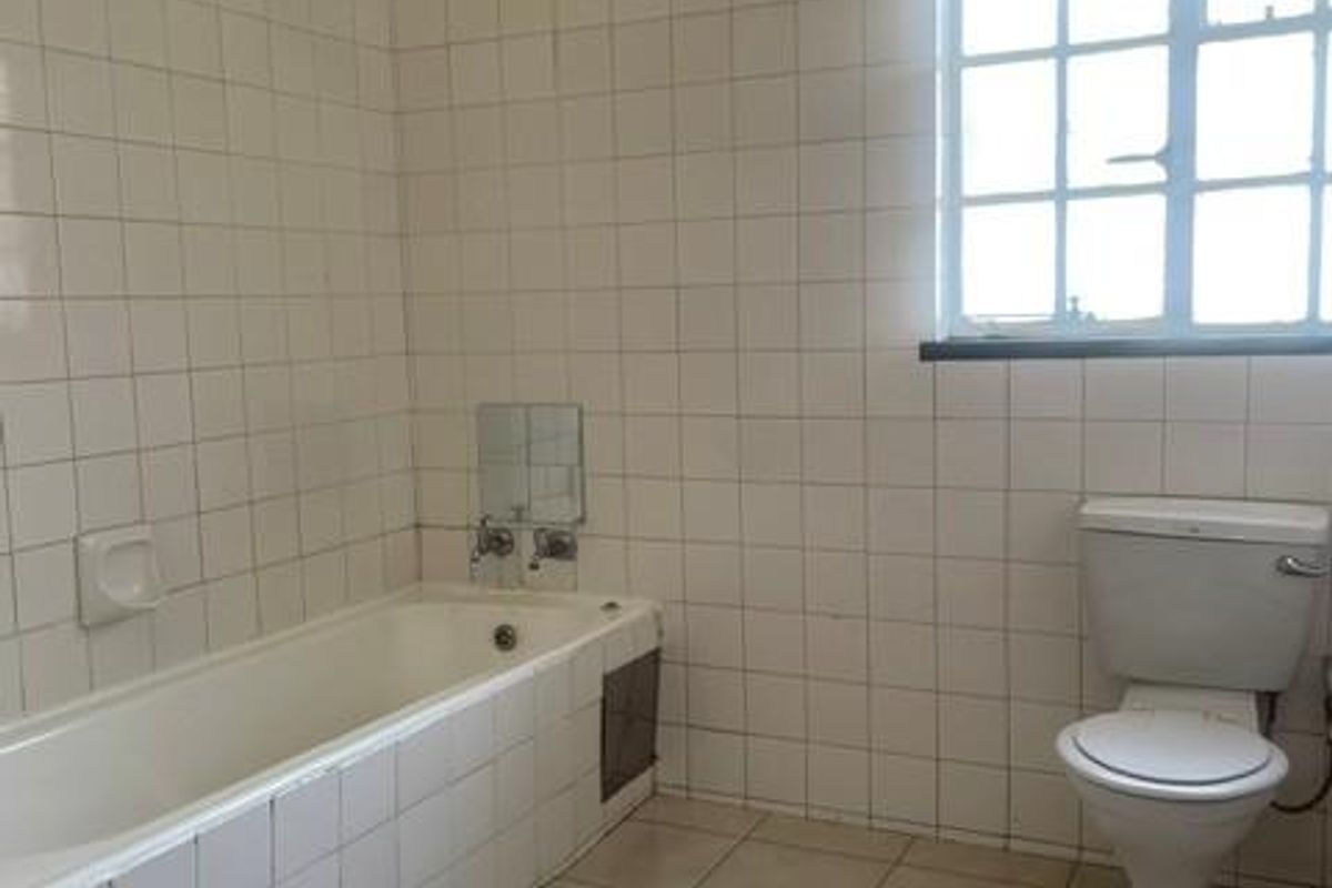 A dated bathroom featuring a tiled bathtub, ceramic toilet, and full-height wall tiling, offering a blank canvas for renovation.