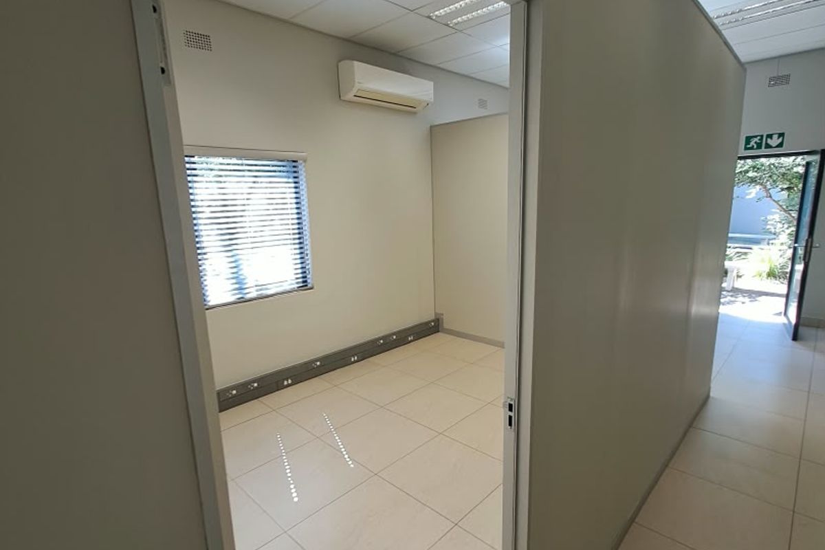 A clean, vacant office space featuring tiled flooring, suspended ceilings with recessed lighting, and a wall-mounted air conditioning unit.