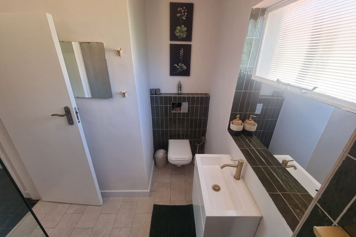 A modern bathroom featuring a wall-hung toilet, a sleek vanity basin with brass fixtures, and dark tiled accents.