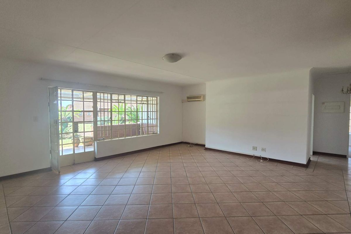 A spacious, empty living area featuring neutral tiled flooring, a wall-mounted air conditioning unit, and a large sliding glass door with security bars.
