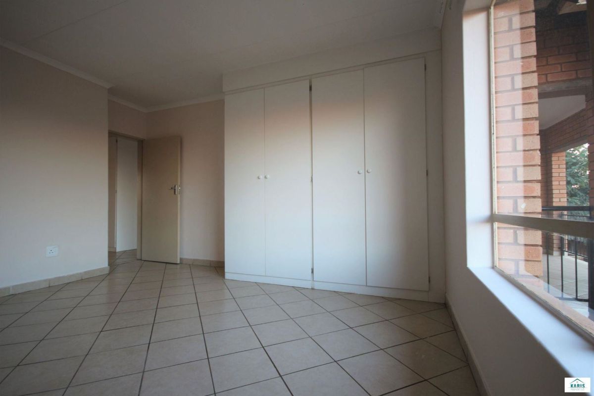 A bright, empty bedroom featuring neutral tiled flooring, built-in wardrobes, and large windows providing natural light.