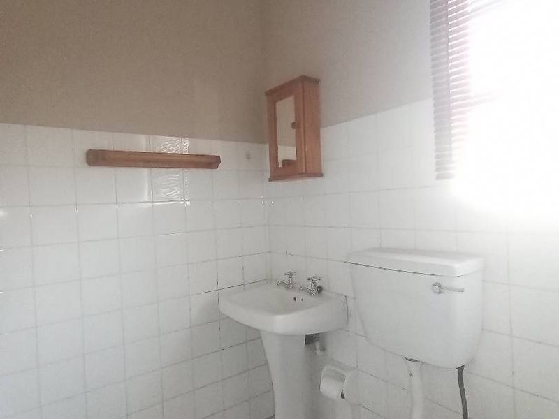 A functional bathroom featuring a pedestal basin, toilet, and tiled finishes, offering a blank canvas for potential modernization and cosmetic updates.