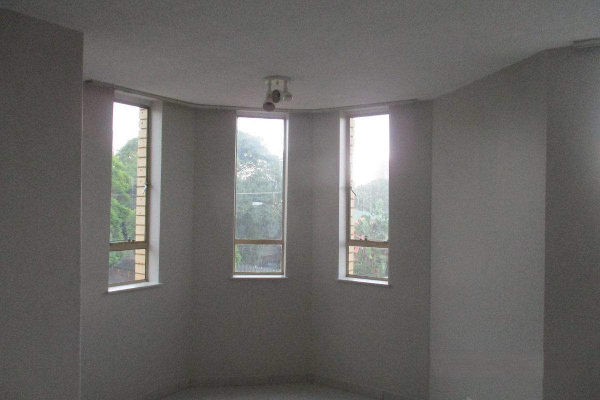 A bright, empty living area featuring large casement windows, neutral wall finishes, and tiled flooring, offering a blank canvas for interior design.