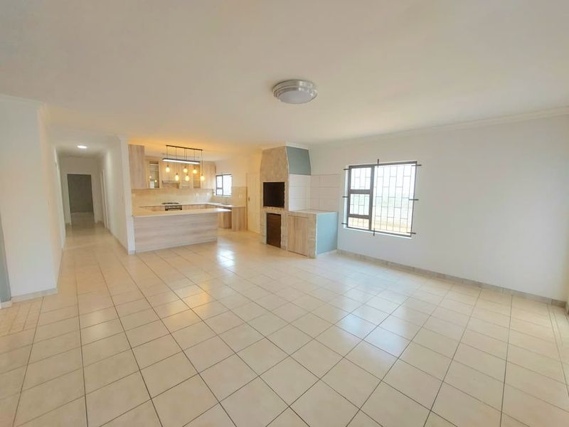 Spacious open-plan living area featuring a built-in fireplace and a modern kitchen with integrated cabinetry and appliances, finished with neutral floor tiles.