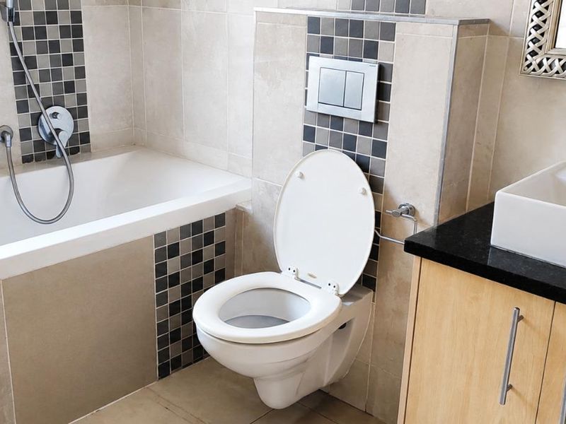 Modern bathroom featuring a built-in bathtub, wall-mounted toilet, and a vanity with a countertop basin, accented by decorative mosaic tiling.