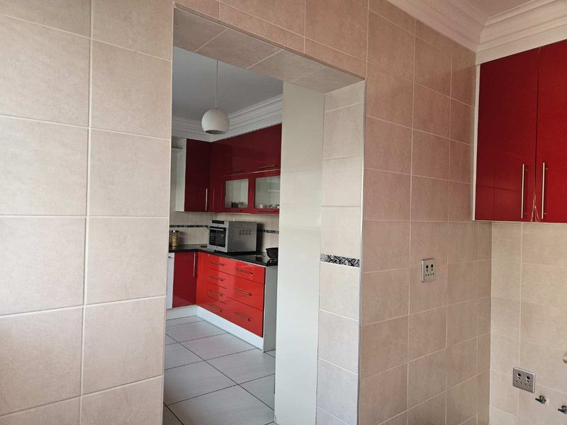 A view through a doorway into a kitchen featuring red high-gloss cabinetry, dark countertops, and neutral wall tiling.