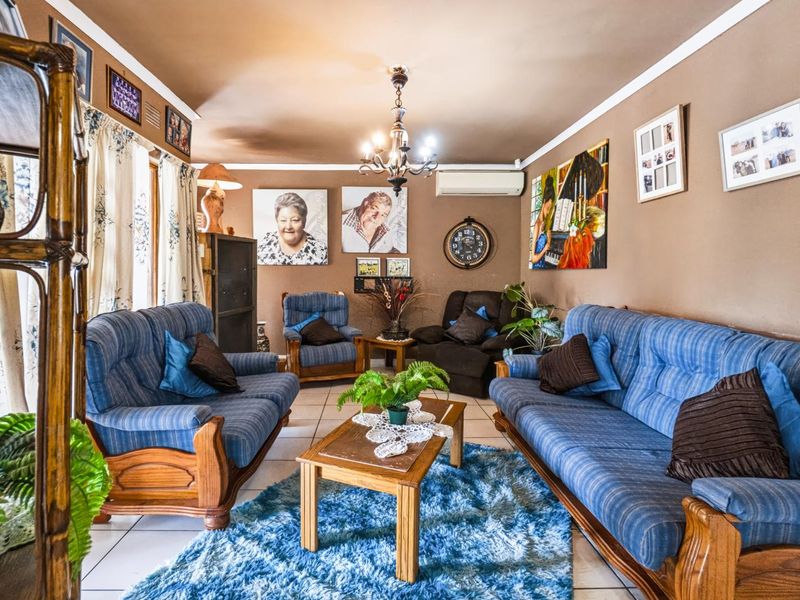 A comfortable living room featuring tiled flooring, a central chandelier, and a wall-mounted split-system air conditioning unit.