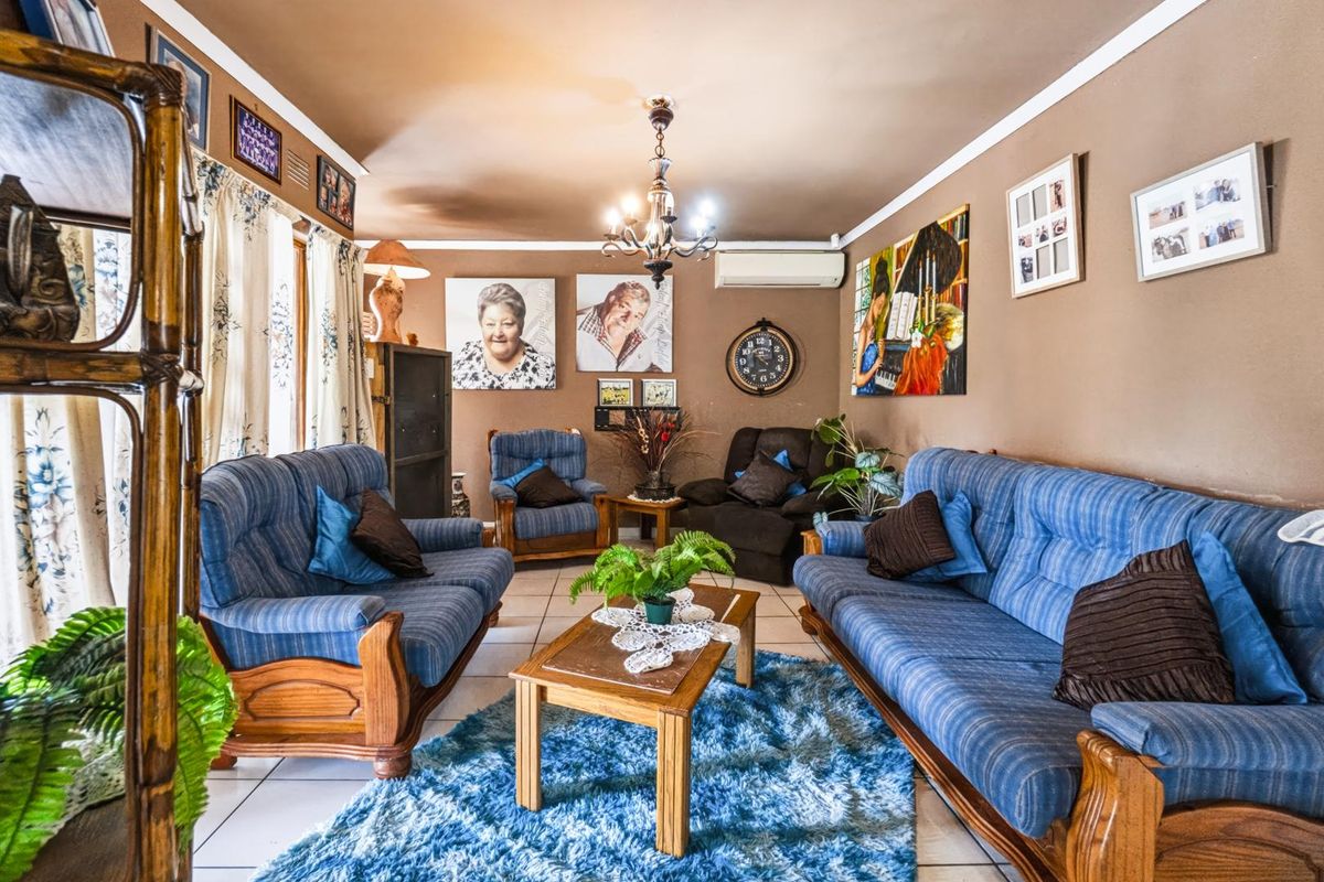 A comfortable living room featuring tiled flooring, a central chandelier, and a wall-mounted split-system air conditioning unit.