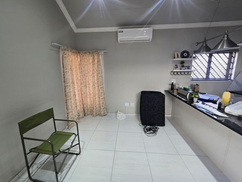 Open plan living area featuring tiled flooring, a granite kitchen breakfast bar, pendant lighting, and a wall-mounted air conditioning unit.