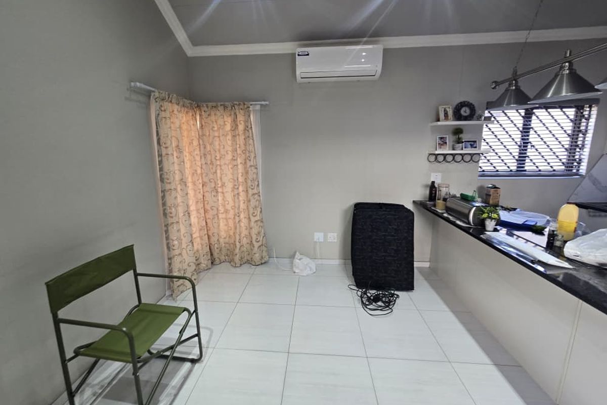 Open plan living area featuring tiled flooring, a granite kitchen breakfast bar, pendant lighting, and a wall-mounted air conditioning unit.