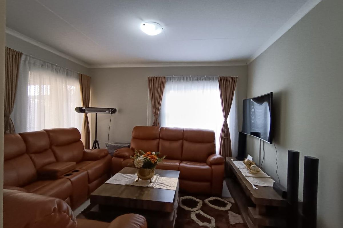 A comfortable living room featuring neutral wall tones, cove cornicing, and ample natural light through large windows.