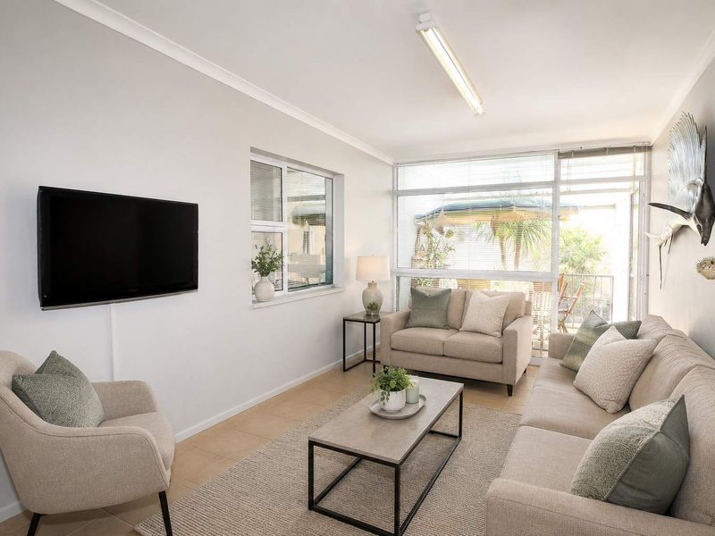 A bright and well-maintained living room featuring tiled flooring, large windows, and a sliding glass door providing access to the outdoor area.