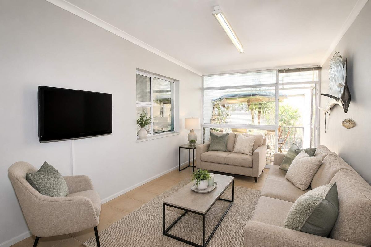 A bright and well-maintained living room featuring tiled flooring, large windows, and a sliding glass door providing access to the outdoor area.