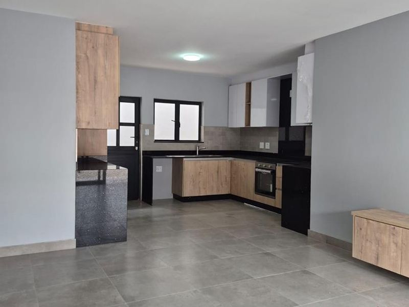 Modern open-plan kitchen featuring wood-grain and high-gloss cabinetry, stone countertops, and integrated appliances, set against a neutral tiled living area.