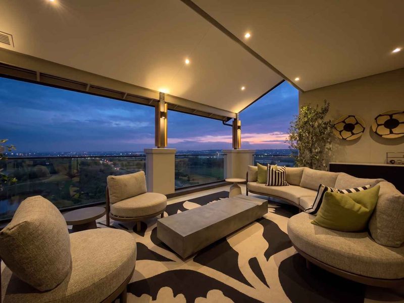 A modern covered balcony featuring a glass balustrade and recessed lighting, offering expansive elevated views at dusk.