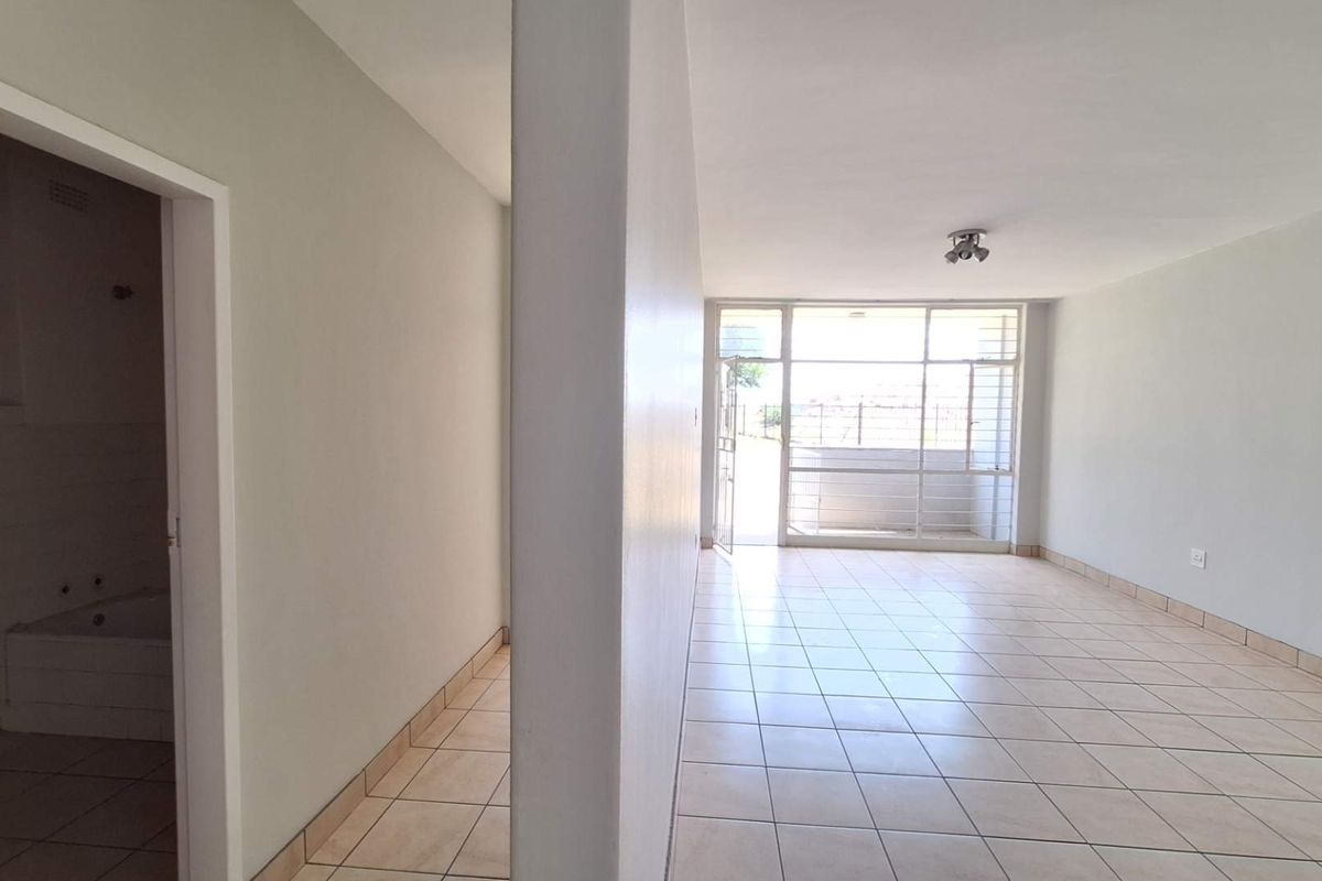 A bright, open-plan living area featuring neutral tiled flooring, large windows, and direct access to an outdoor space.