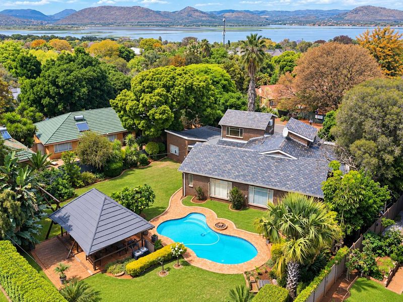 Aerial view of a residential property featuring a swimming pool, gazebo, landscaped garden, and tiled roof, set against a scenic lake and mountain backdrop.