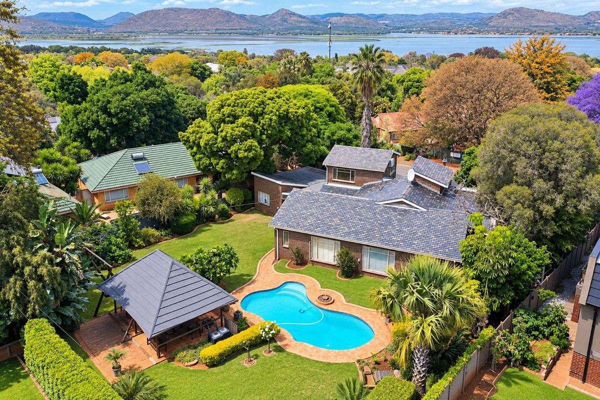 Aerial view of a residential property featuring a swimming pool, gazebo, landscaped garden, and tiled roof, set against a scenic lake and mountain backdrop.