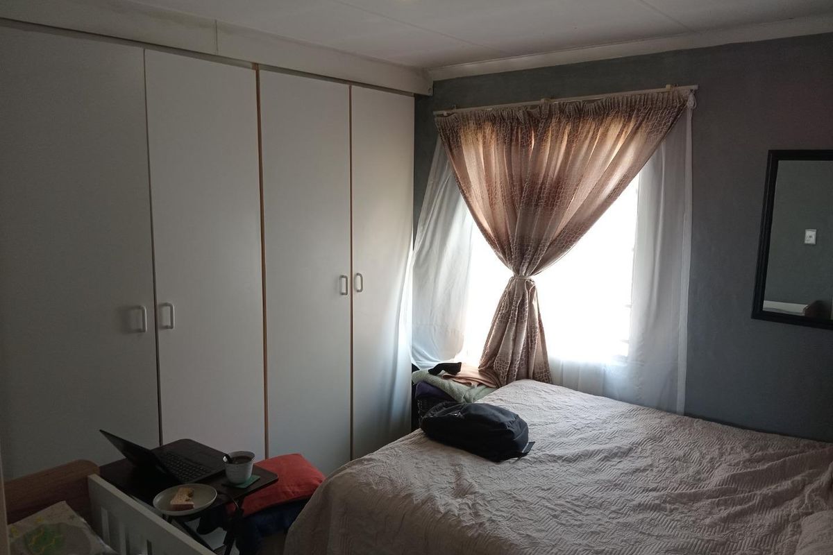 A bedroom featuring built-in cupboards and a window with curtains, providing functional storage and natural light.