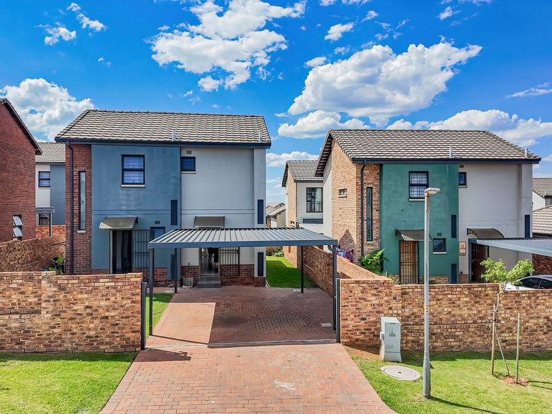 Front view of modern semi-detached residential homes featuring brick boundary walls, paved driveways, and integrated carports under a clear blue sky.