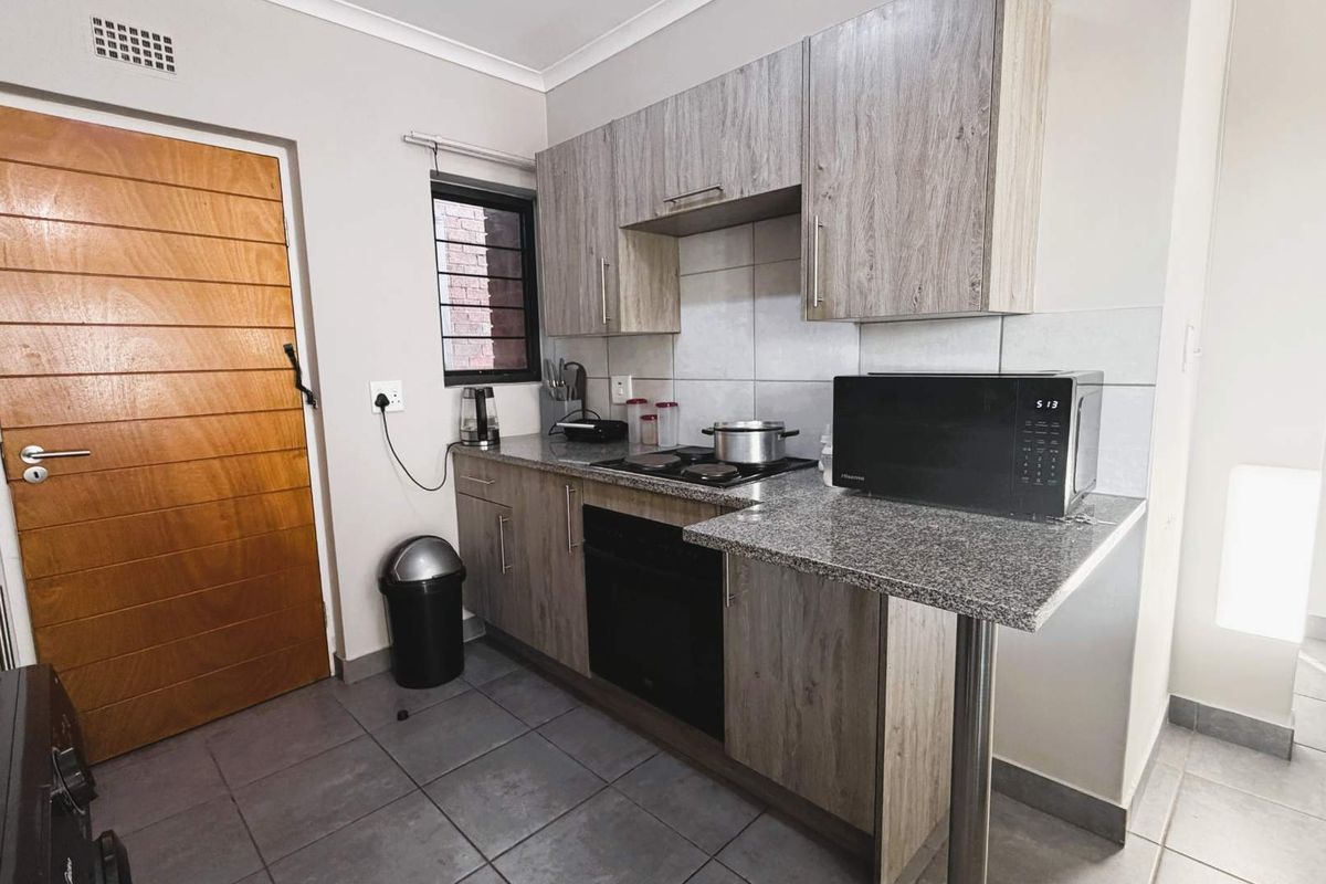 A functional kitchen featuring wood-look cabinetry, granite countertops, a built-in oven, and a hob, complemented by tiled flooring and a breakfast bar.