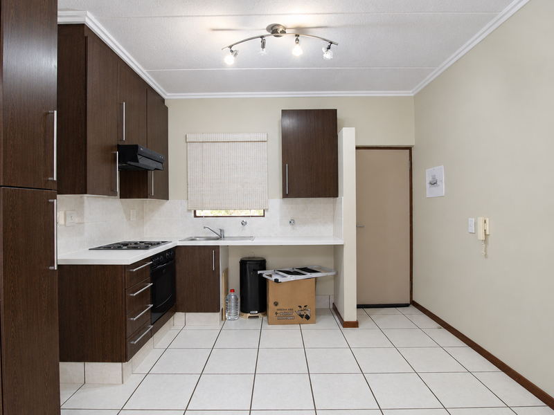 A functional kitchen featuring dark wood cabinetry, built-in oven, gas hob, extractor fan, and tiled flooring, offering a clean and practical workspace.