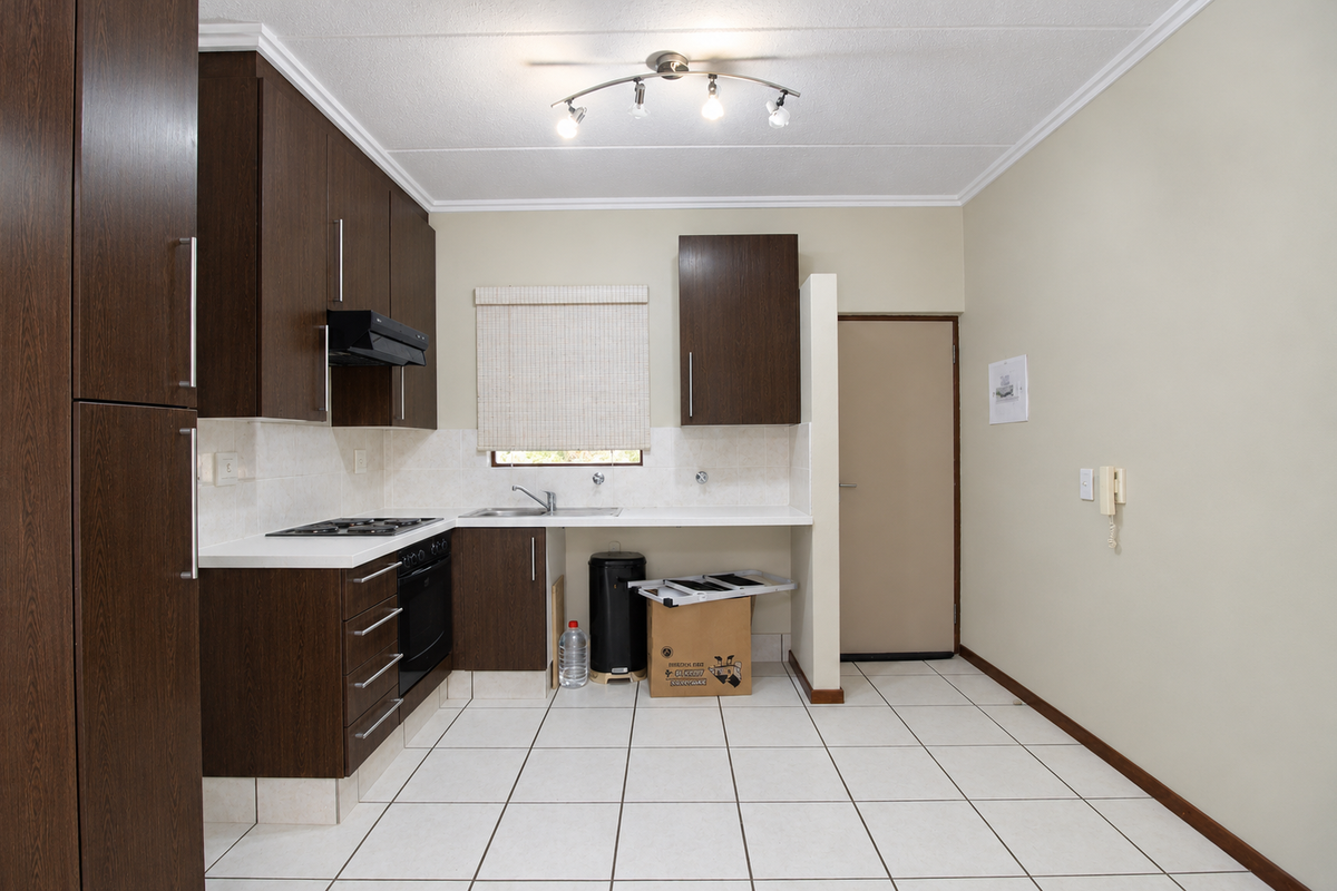 A functional kitchen featuring dark wood cabinetry, built-in oven, gas hob, extractor fan, and tiled flooring, offering a clean and practical workspace.