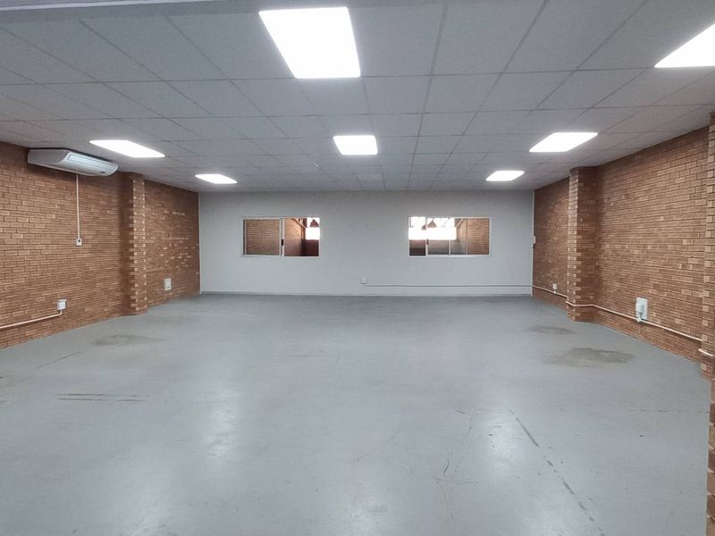 Spacious industrial open-plan area featuring exposed brick walls, suspended ceiling with recessed lighting, and durable painted concrete flooring.