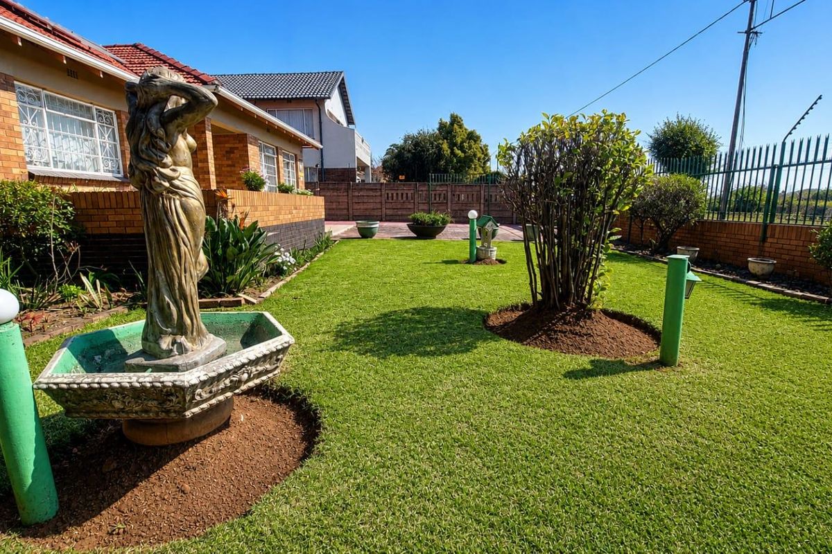 A well-maintained rear garden featuring a manicured lawn, established landscaping, and a brick boundary wall with security fencing.