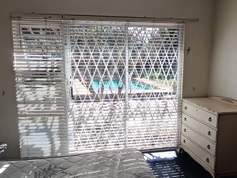 Bedroom featuring a sliding glass door with security gate and venetian blinds, offering a view of the outdoor pool area.