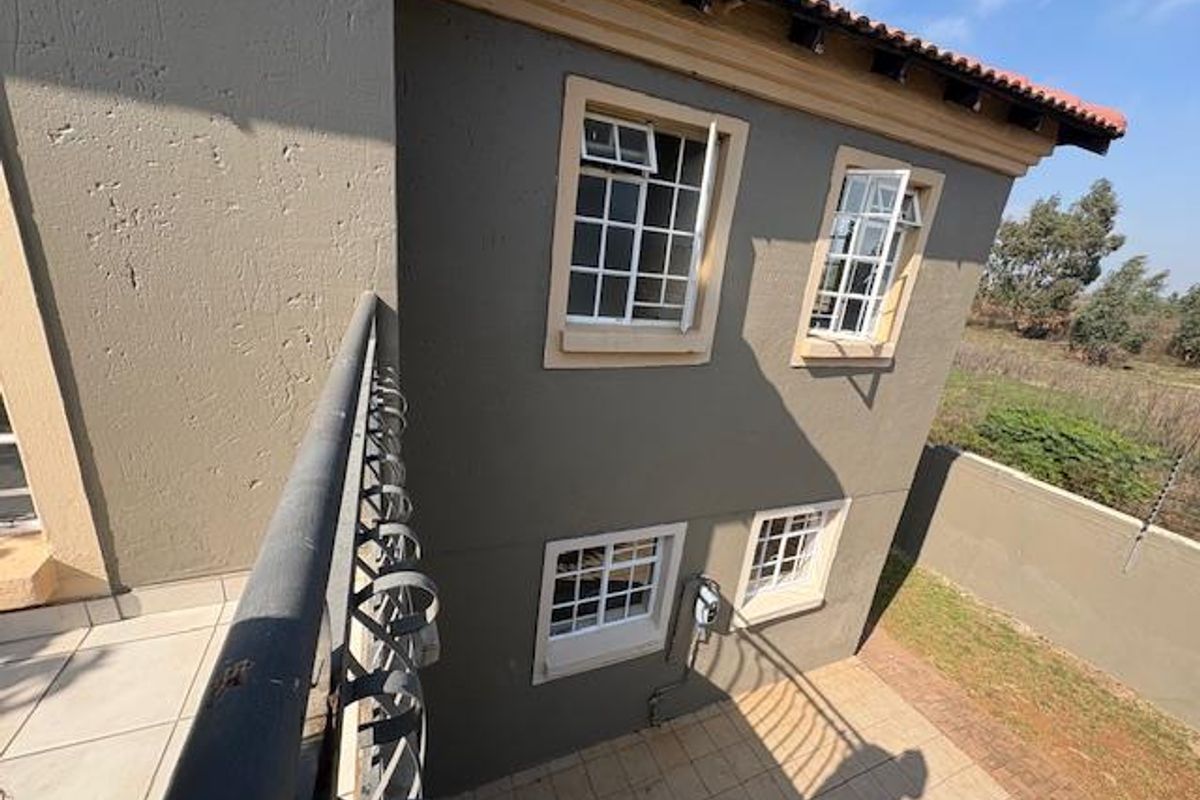 View from an upper-level balcony overlooking the rear exterior facade, tiled patio area, and surrounding garden space of the townhouse.