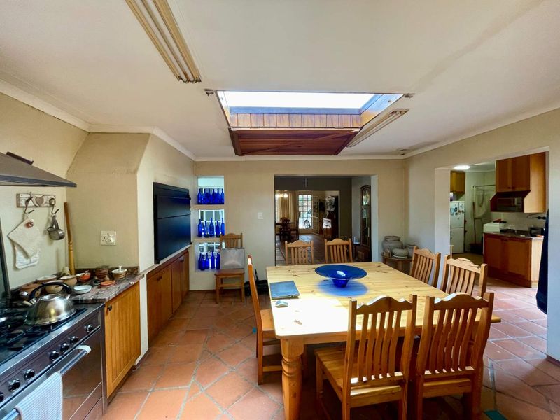 Open-plan kitchen and dining area featuring terracotta flooring, a central skylight, and built-in cabinetry with integrated cooking appliances.