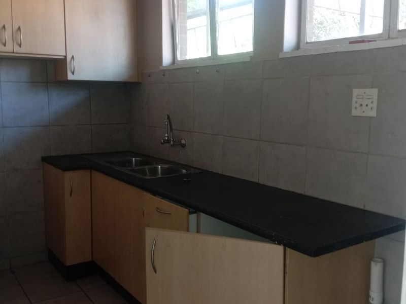 A functional kitchen area featuring laminate cabinetry, a double bowl sink, and tiled splashbacks, currently requiring minor repairs to cabinetry.