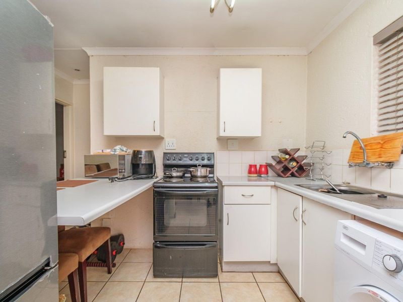 A functional kitchen featuring white cabinetry, laminate countertops, a stainless steel sink, and a freestanding stove with tiled flooring.