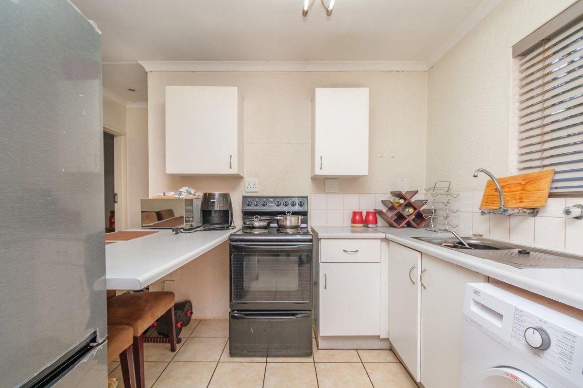 A functional kitchen featuring white cabinetry, laminate countertops, a stainless steel sink, and a freestanding stove with tiled flooring.