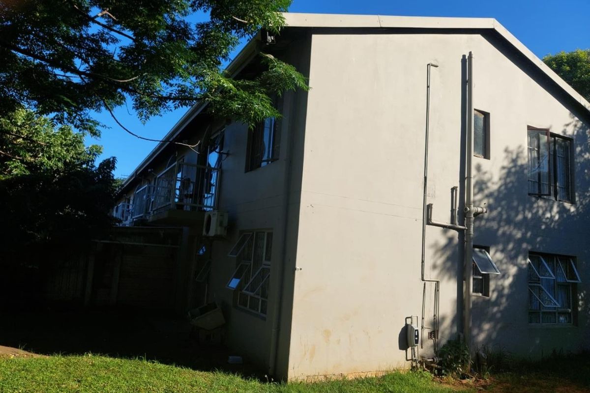 Rear view of a multi-story residential building featuring external plumbing, casement windows, and a small balcony.