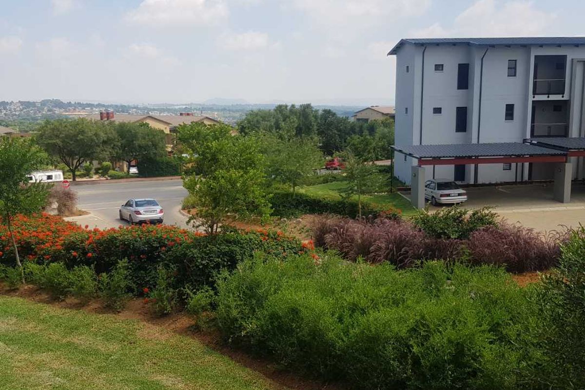 An elevated view of the apartment complex exterior, featuring landscaped gardens, a covered parking area, and surrounding neighborhood views.