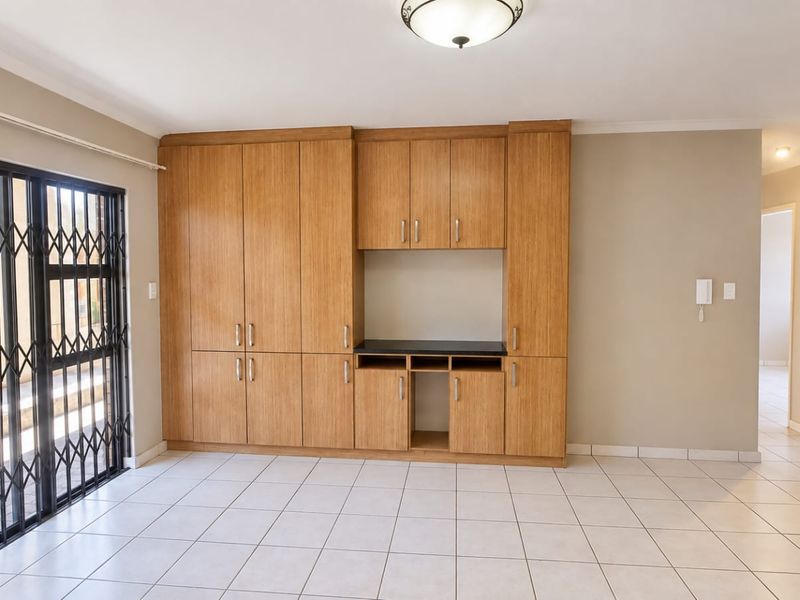 Spacious living area featuring neutral tiled flooring, extensive built-in wooden cabinetry, and a secure sliding door access to the exterior.